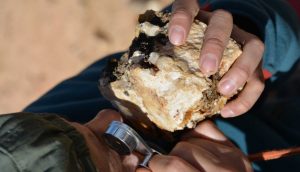 Géologue observant à la loupe un échantillon de roche minéralisée